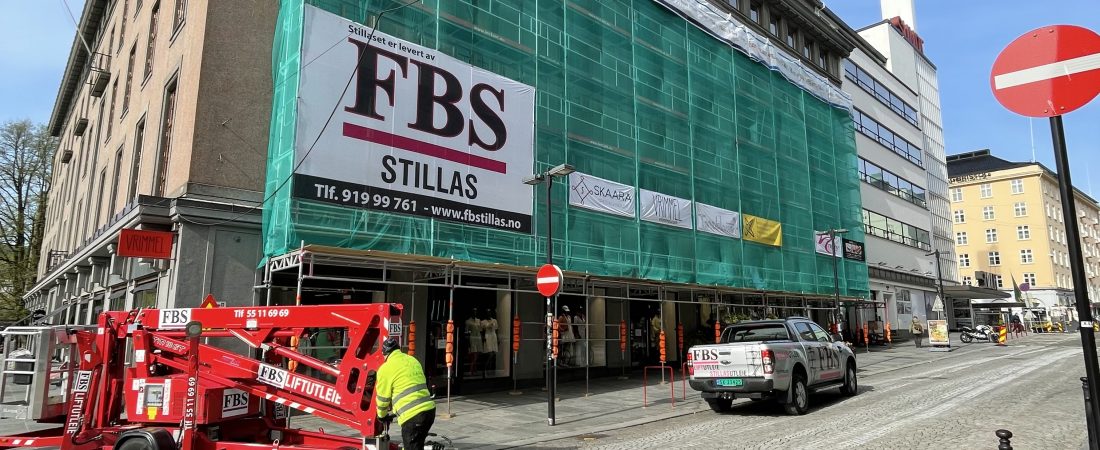 Image of a large building with a large scaffold on the fasade covered by a green net. Scaffold delivered by FBS. FBS - spesialist på lift og stillas.