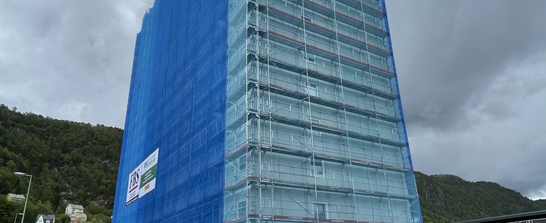 Picture showing a high building completely covered by scaffold with a blue net, delivered by FBS | Bildet viser en høyblokk kledd inn i stillas med blå not fra FBS